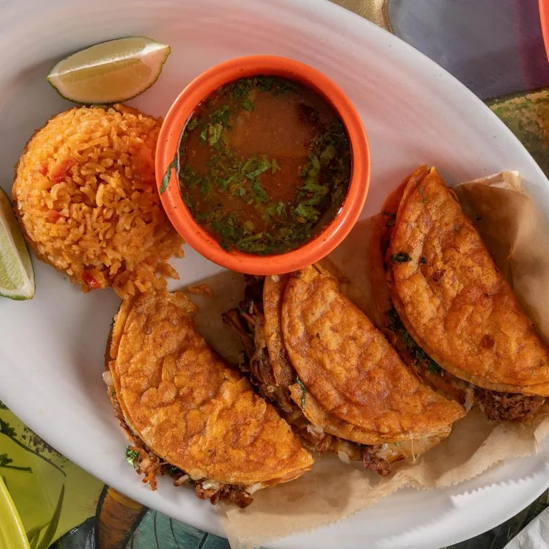 Golden crispy tacos with rice and a cup of consomé